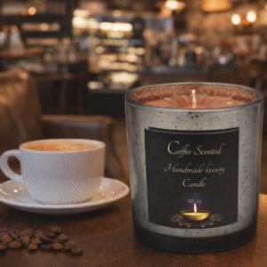 Coffee scented handmade luxury candle in a speckled gray glass jar with black and gold label, displayed on a soft pink background.