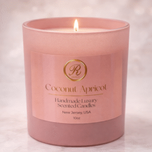 A handmade luxury Coconut Apricot candle in a frosted blush glass jar, softly glowing on a white stone countertop in a modern kitchen, illuminated by warm candlelight for an elegant, cozy ambiance.